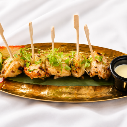 Skewered tender grilled chicken tikka garnished with microgreens, served on a golden platter.