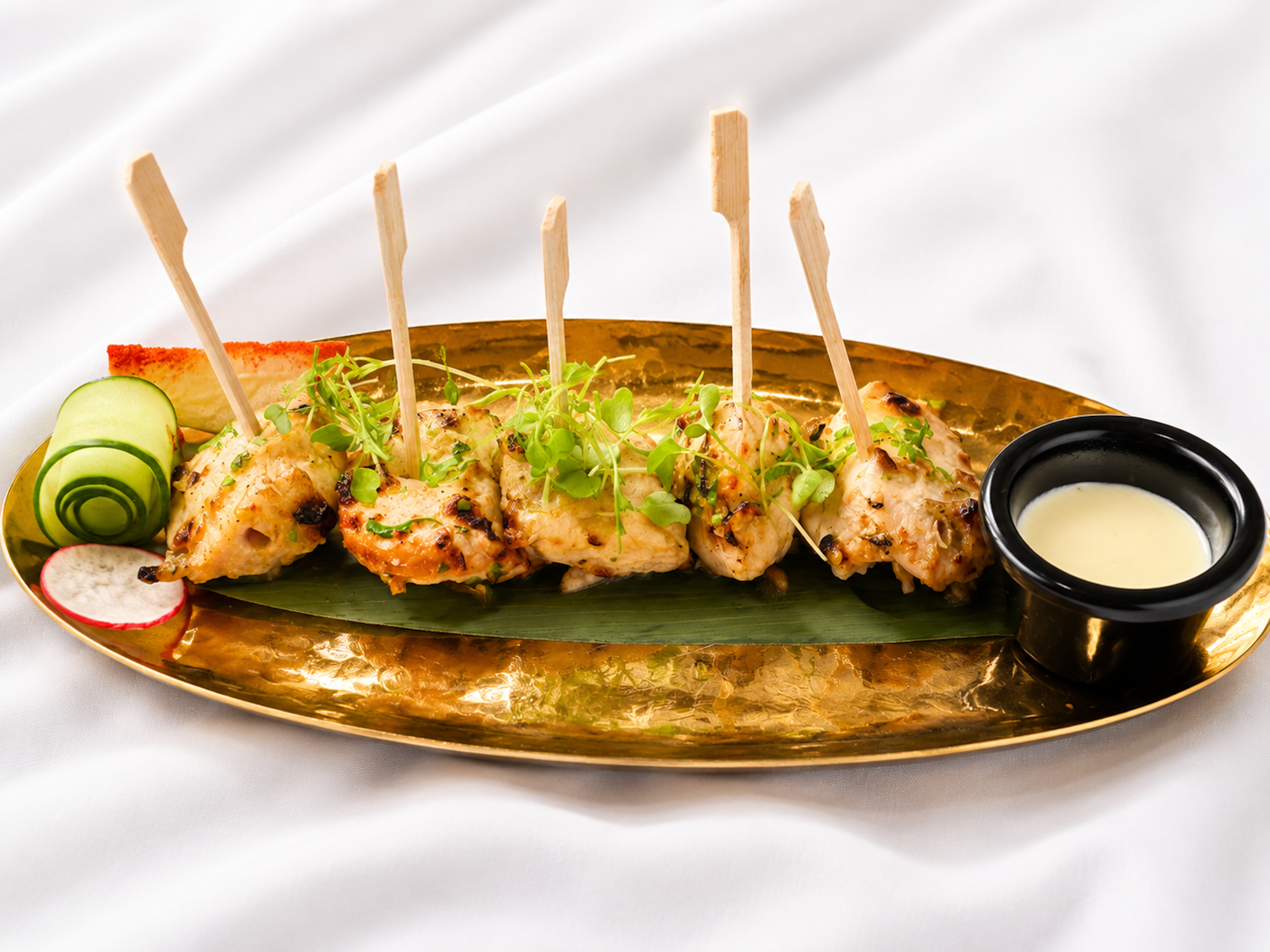 Skewered tender grilled chicken tikka garnished with microgreens, served on a golden platter.