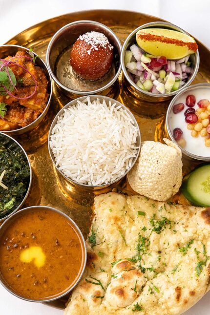 Traditional Thali platter from the set lunch menu, featuring basmati rice, garlic naan, assorted curries, dal, and gulab jamun on a brass plate.