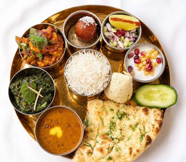 Traditional Thali platter from the set lunch menu, featuring basmati rice, garlic naan, assorted curries, dal, and gulab jamun on a brass plate.