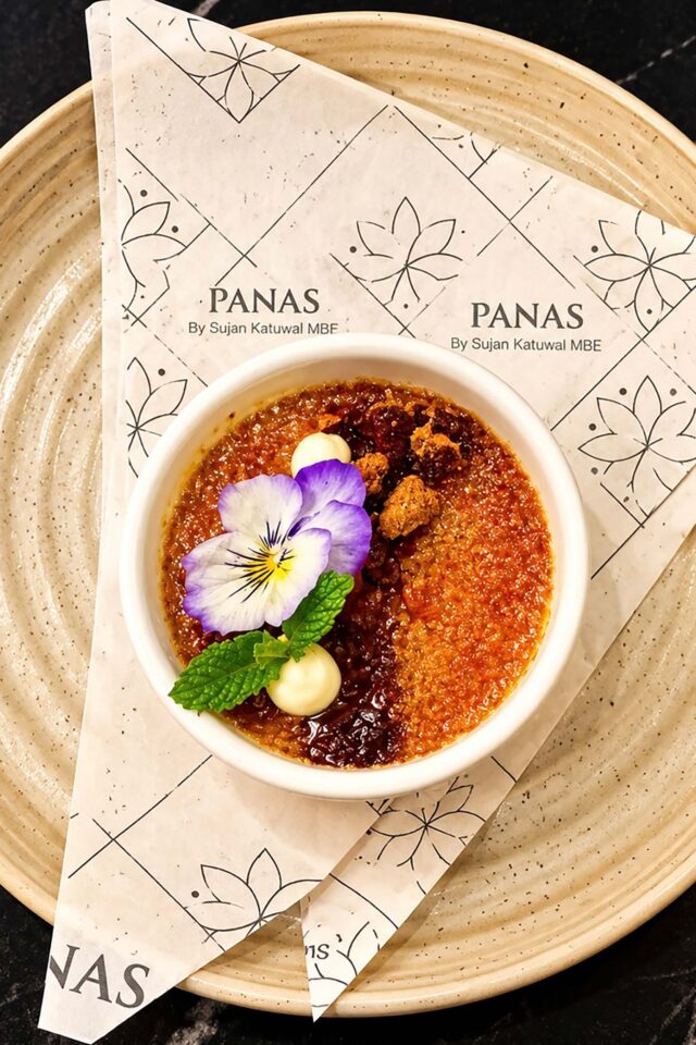 A beautifully garnished crème brûlée topped with an edible flower and mint, served on branded paper at Panas Restaurant by Sujan Katuwal MBE