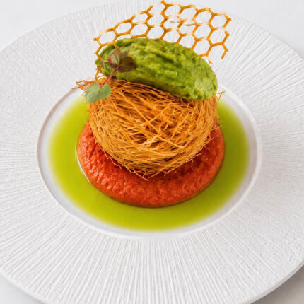 An elegant kataifi-wrapped appetizer resting on a vibrant red sauce, topped with green puree and a delicate honeycomb tuile at Panas Restaurant.