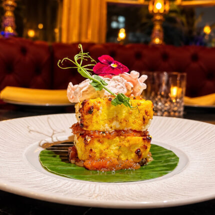 A beautifully stacked paneer dish resting on a green banana leaf, topped with an edible purple flower in the ambient dining room of Panas Restaurant