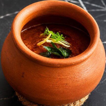 A rich, aromatic curry served in a traditional clay pot and garnished with fresh herbs at Panas Restaurant