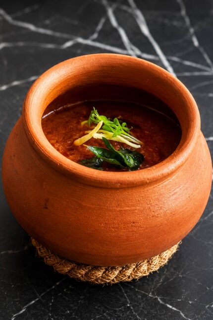 A rich, aromatic curry served in a traditional clay pot and garnished with fresh herbs at Panas Restaurant.