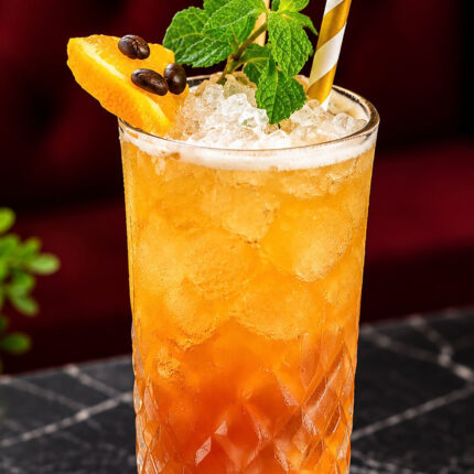 A refreshing iced orange cocktail garnished with mint, an orange slice, and coffee beans served at Panas Restaurant.