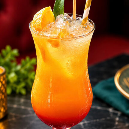 A vibrant, layered tropical cocktail served in a hurricane glass over crushed ice with a citrus and leaf garnish at Panas Restaurant.